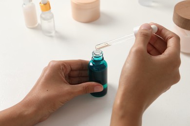 Woman with bottle of cosmetic serum at white table, closeup