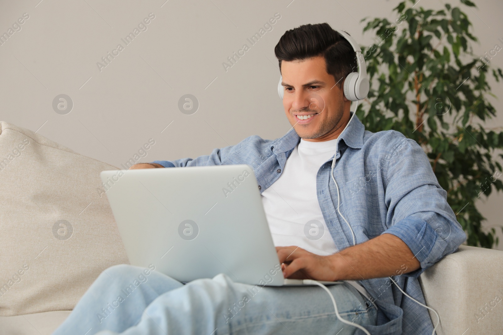 Photo of Man with laptop and headphones sitting on sofa at home