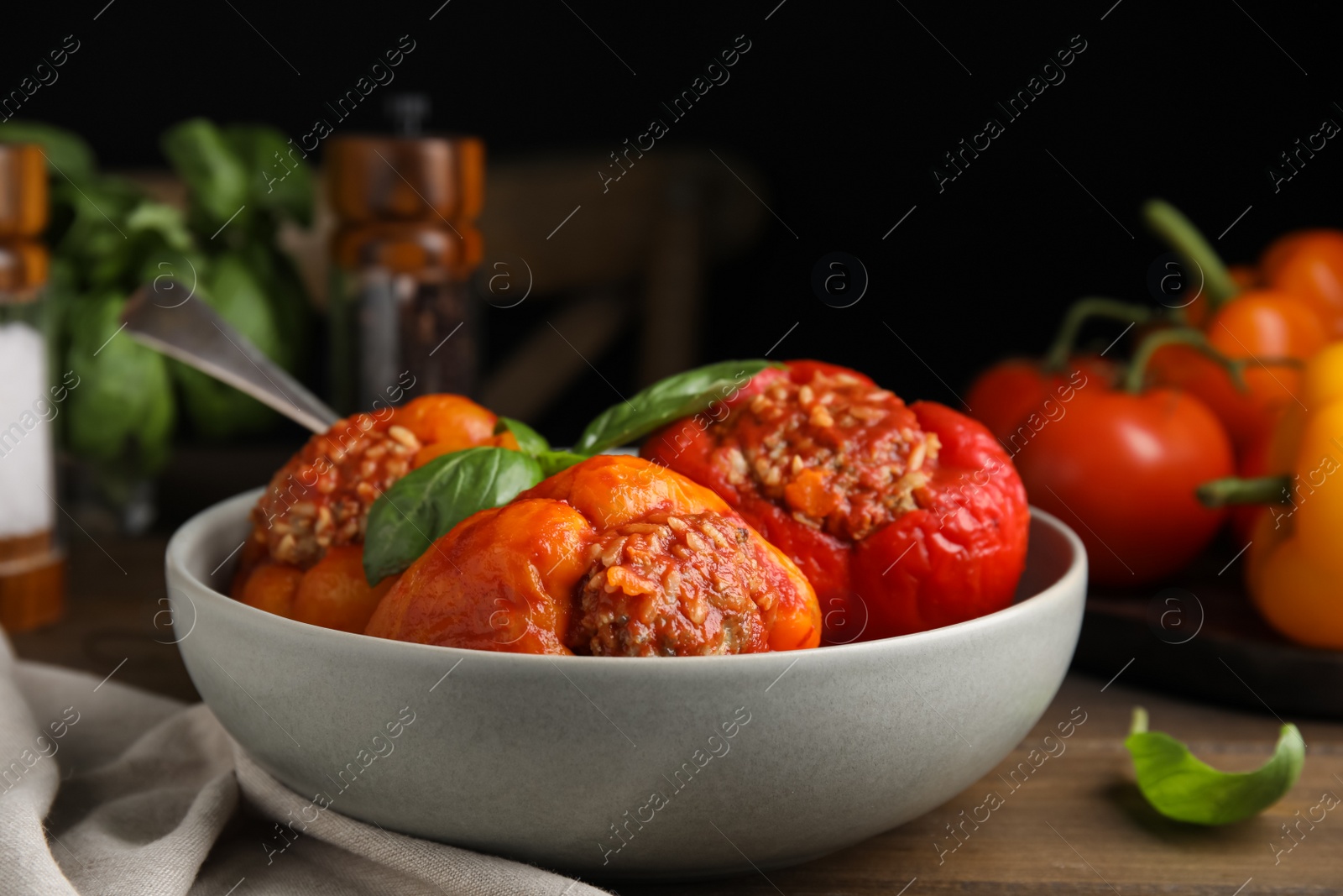 Photo of Delicious stuffed peppers with basil in bowl on wooden table