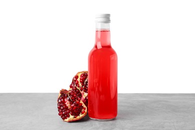 Delicious kombucha in glass bottle and pomegranate on grey table against white background