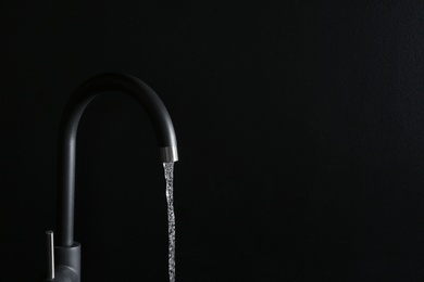 Photo of Closeup view of water flowing from faucet on black background. Space for text