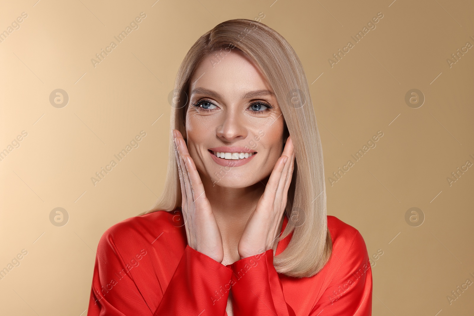 Image of Portrait of stylish attractive woman with blonde hair smiling on dark beige background