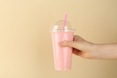 Woman with plastic cup of tasty smoothie on beige background, closeup