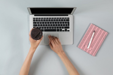 Woman with cup of coffee using modern laptop, top view