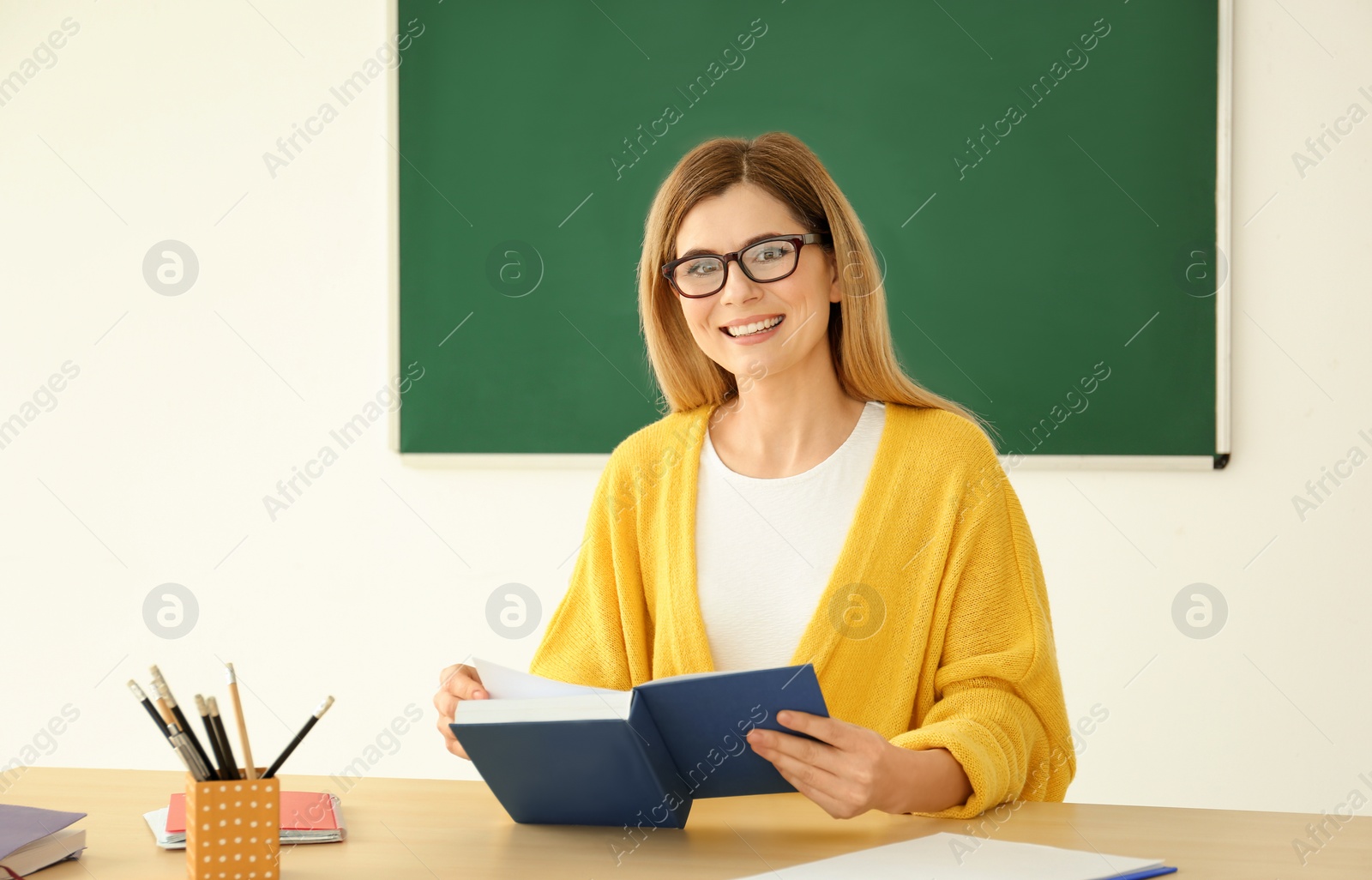 Photo of Young female teacher working at table in classroom