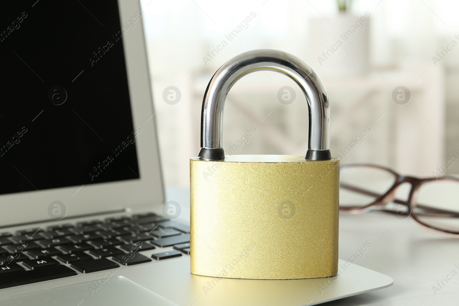 Photo of Metal lock and laptop on table, closeup. Protection from cyber attack