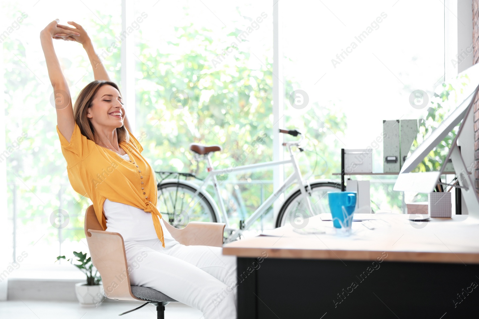 Photo of Beautiful young businesswoman stretching in office. Workplace fitness