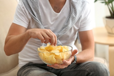 Photo of Man with bowl of potato chips sitting on sofa, closeup