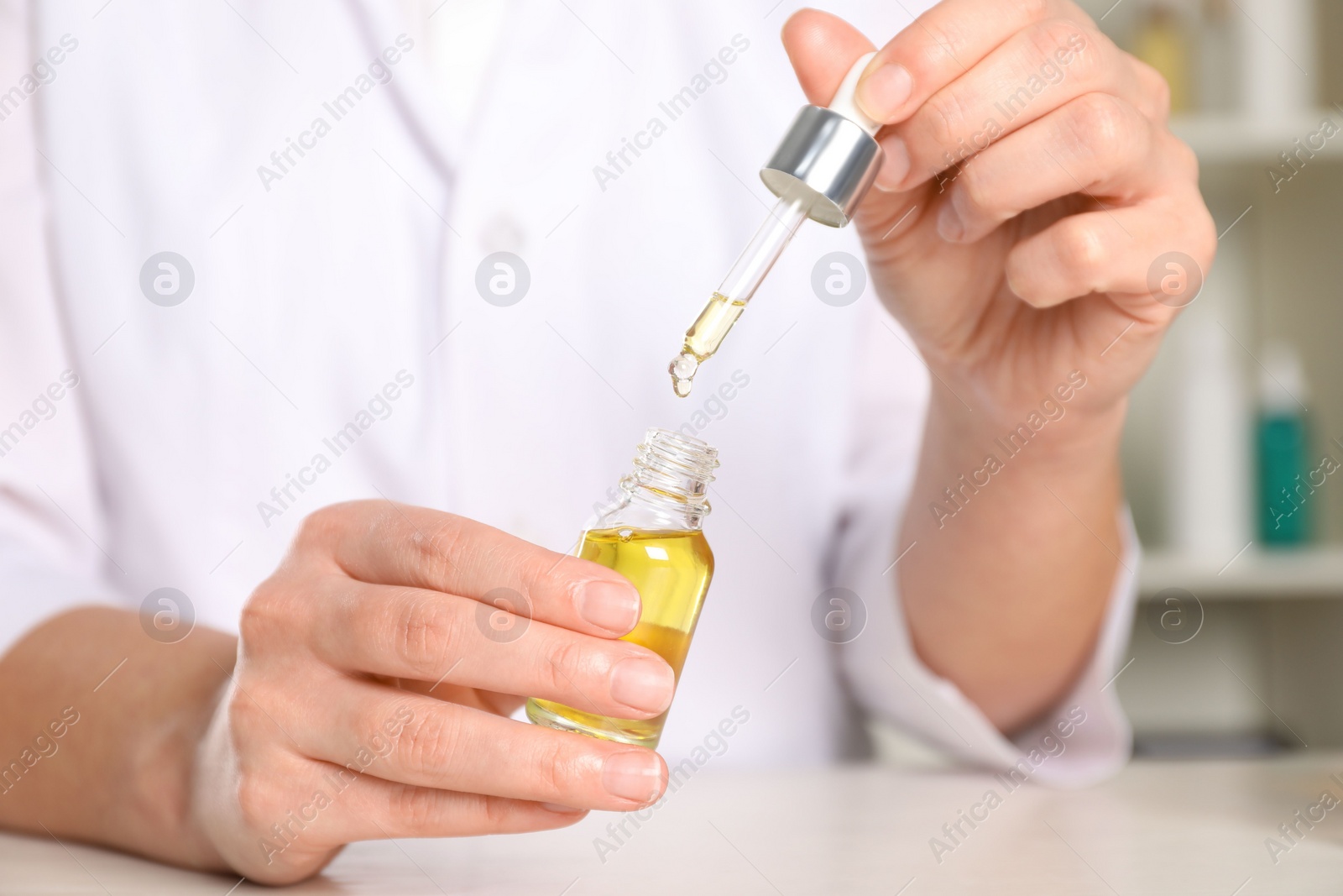 Photo of Dermatologist developing cosmetic oil at white table indoors, closeup