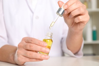 Photo of Dermatologist developing cosmetic oil at white table indoors, closeup