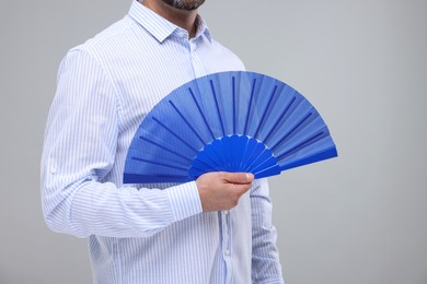 Photo of Man holding hand fan on light grey background, closeup