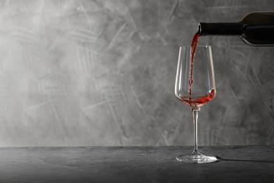 Photo of Pouring red wine from bottle into glass on table. Space for text