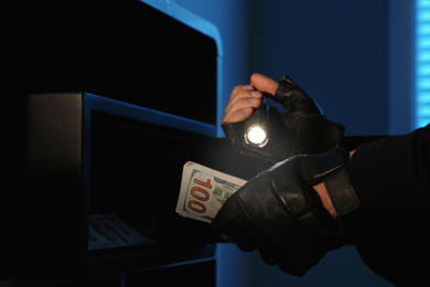 Thief taking money out of steel safe indoors at night, closeup