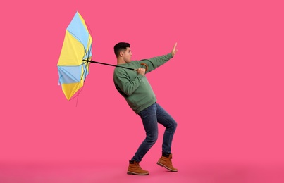 Emotional man with umbrella caught in gust of wind on pink background