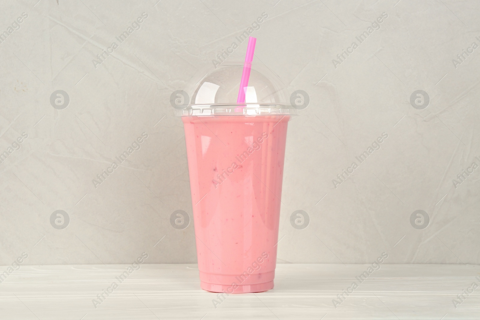 Photo of Plastic cup of tasty strawberry smoothie on white wooden table