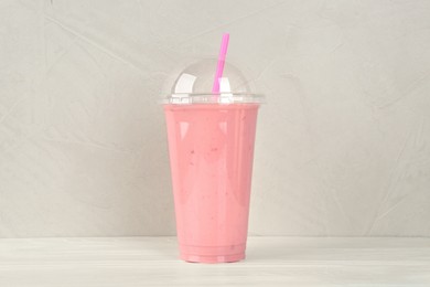 Photo of Plastic cup of tasty strawberry smoothie on white wooden table