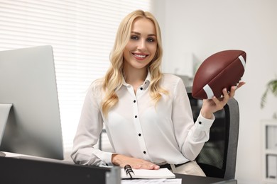 Happy woman with american football ball at table in office