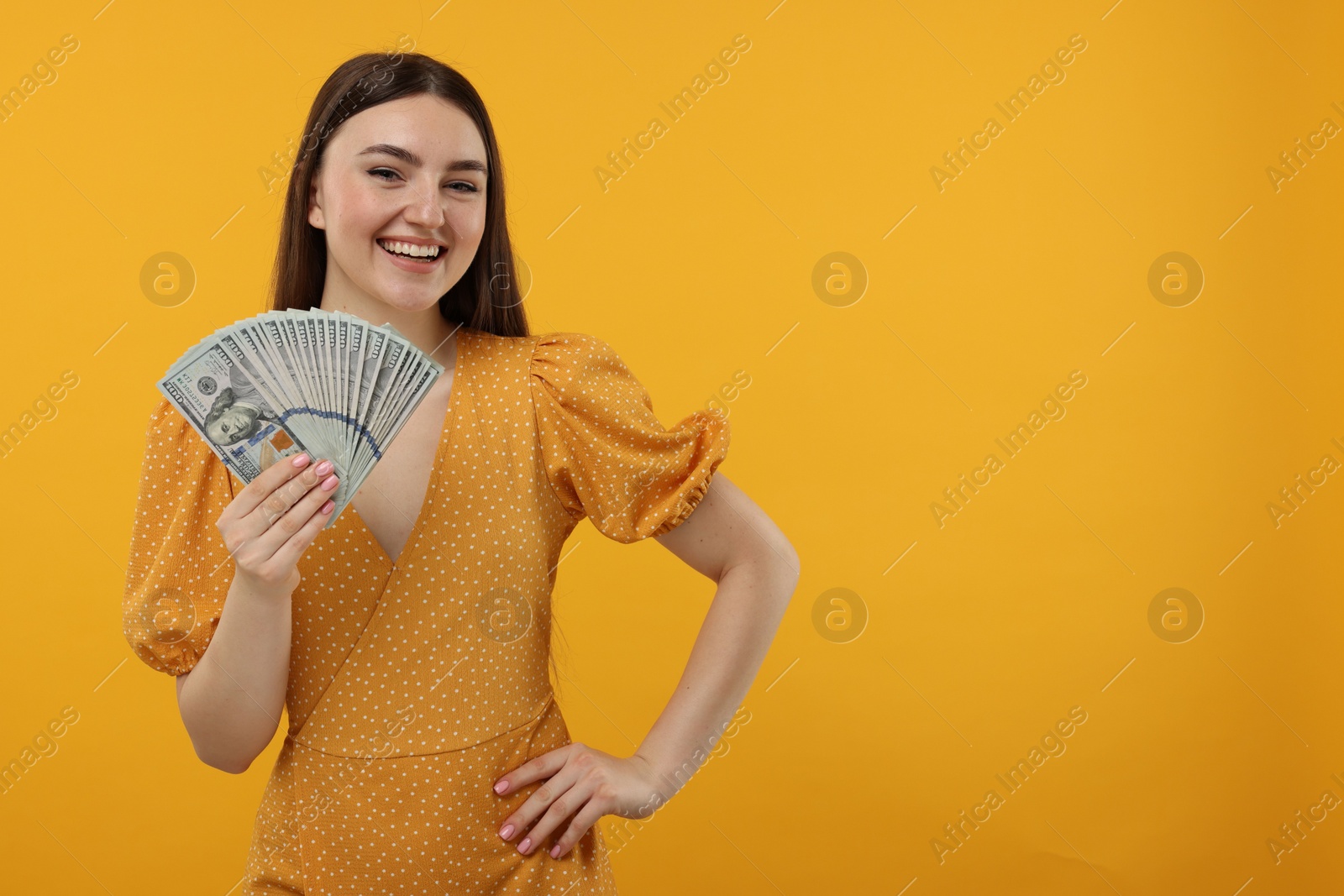 Photo of Happy woman with dollar banknotes on orange background, space for text