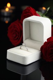 Photo of Beautiful engagement ring with gemstone in box and roses on black background