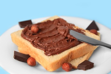 Photo of Spreading chocolate paste onto bread on light blue background, closeup