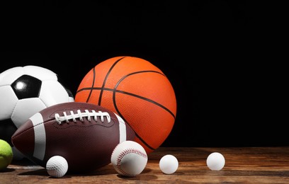Photo of Many different sport balls on wooden table against black background, space for text