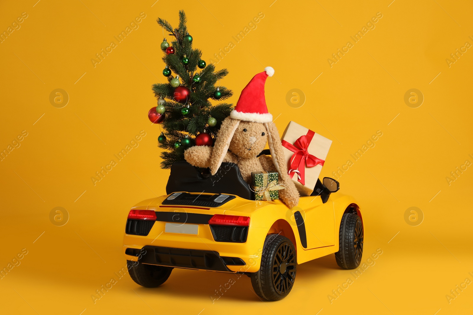 Photo of Child's electric car with toys, gift boxes and Christmas tree on orange background