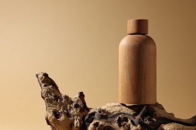 Photo of Wooden bottlecosmetic product on tree bark against dark beige background, space for text