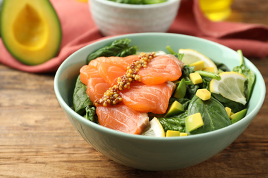 Photo of Delicious salmon with spinach, avocado and lemon in bowl on wooden table