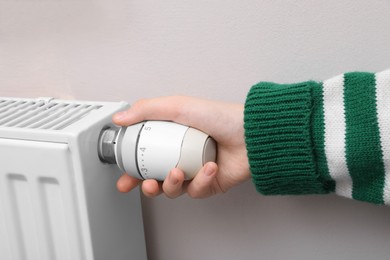 Photo of Girl adjusting heating radiator thermostat near white wall indoors, closeup