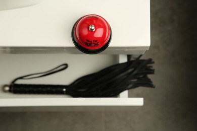 Photo of Red bell and black whip in drawer indoors, selective focus. Sex toys