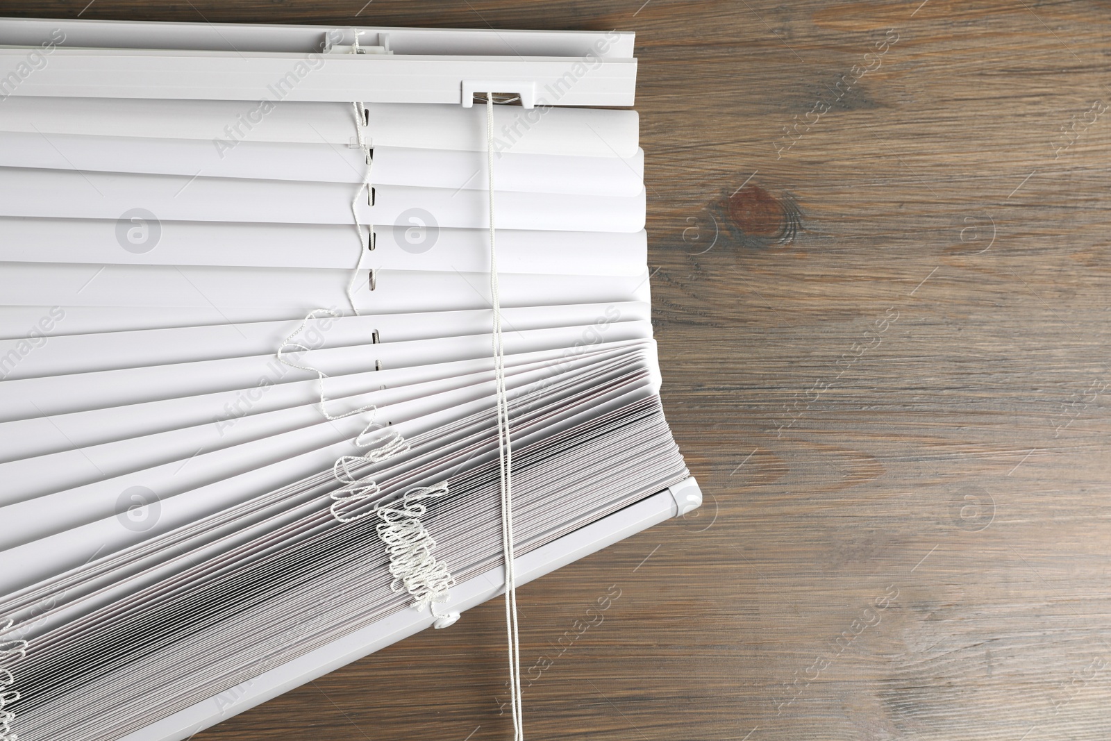 Photo of Stylish horizontal window blinds on wooden table, top view. Space for text