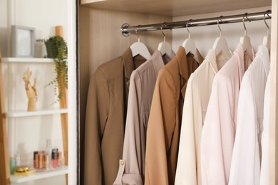 Photo of New stylish clothes hanging in wardrobe, closeup view