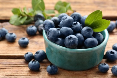 Tasty fresh blueberries and green leaves on wooden table, closeup