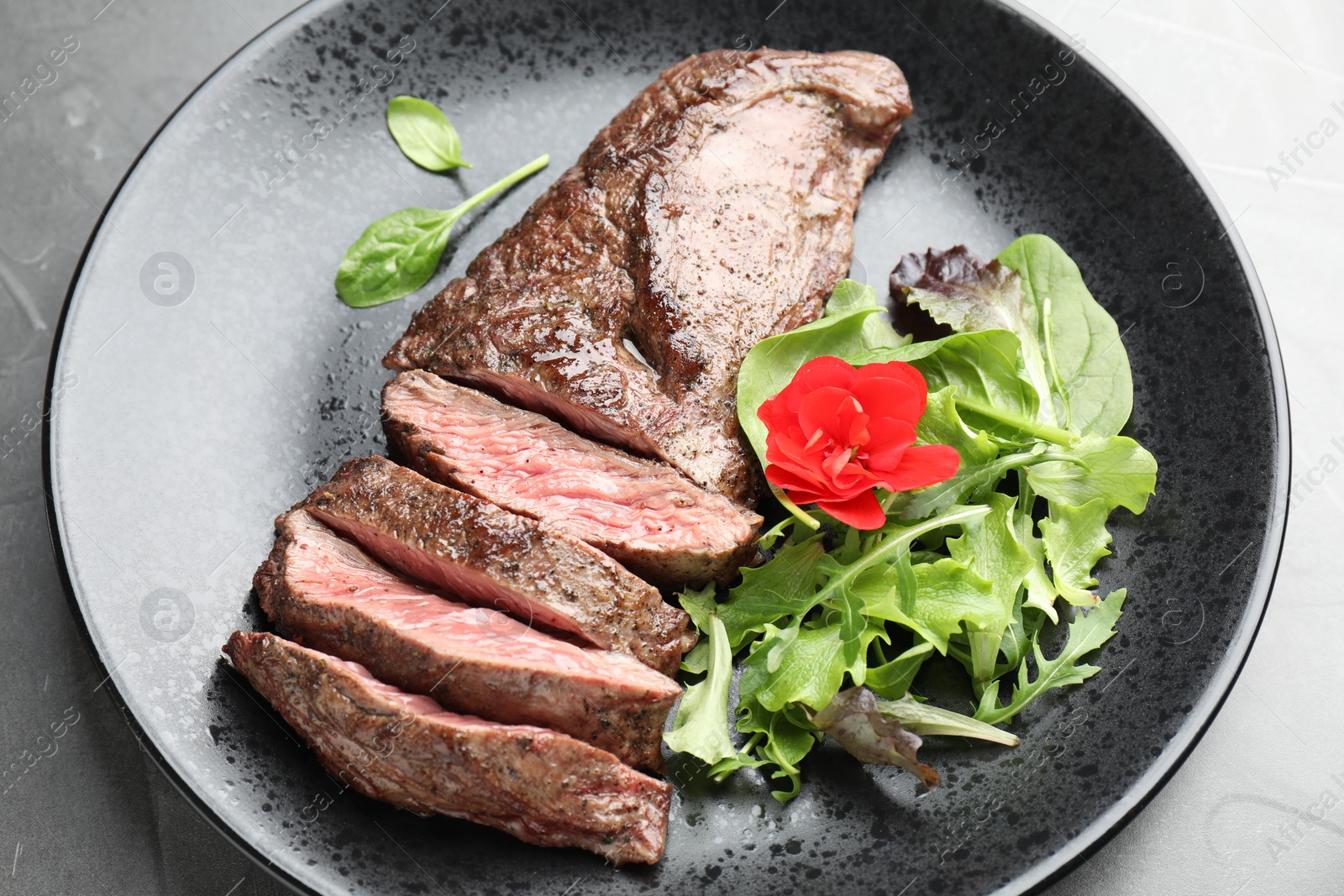 Photo of Pieces of delicious grilled beef meat and greens on grey table, closeup