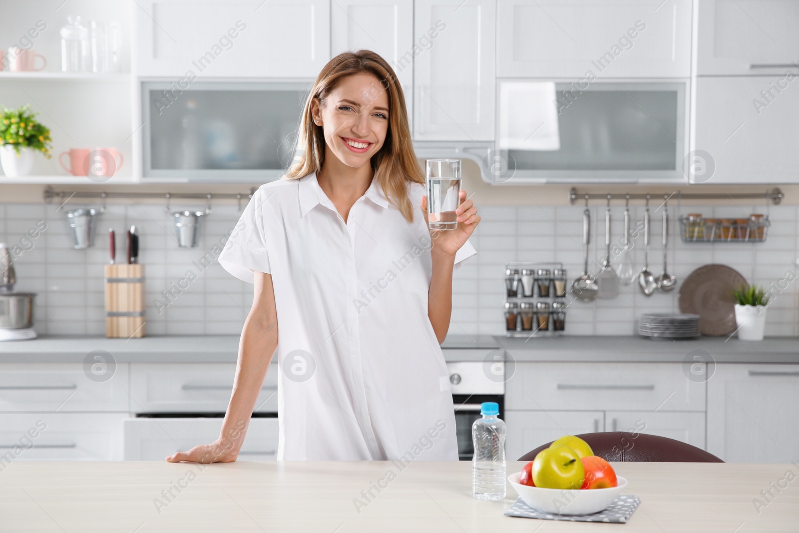 Photo of Young woman holding glass with clean water in kitchen