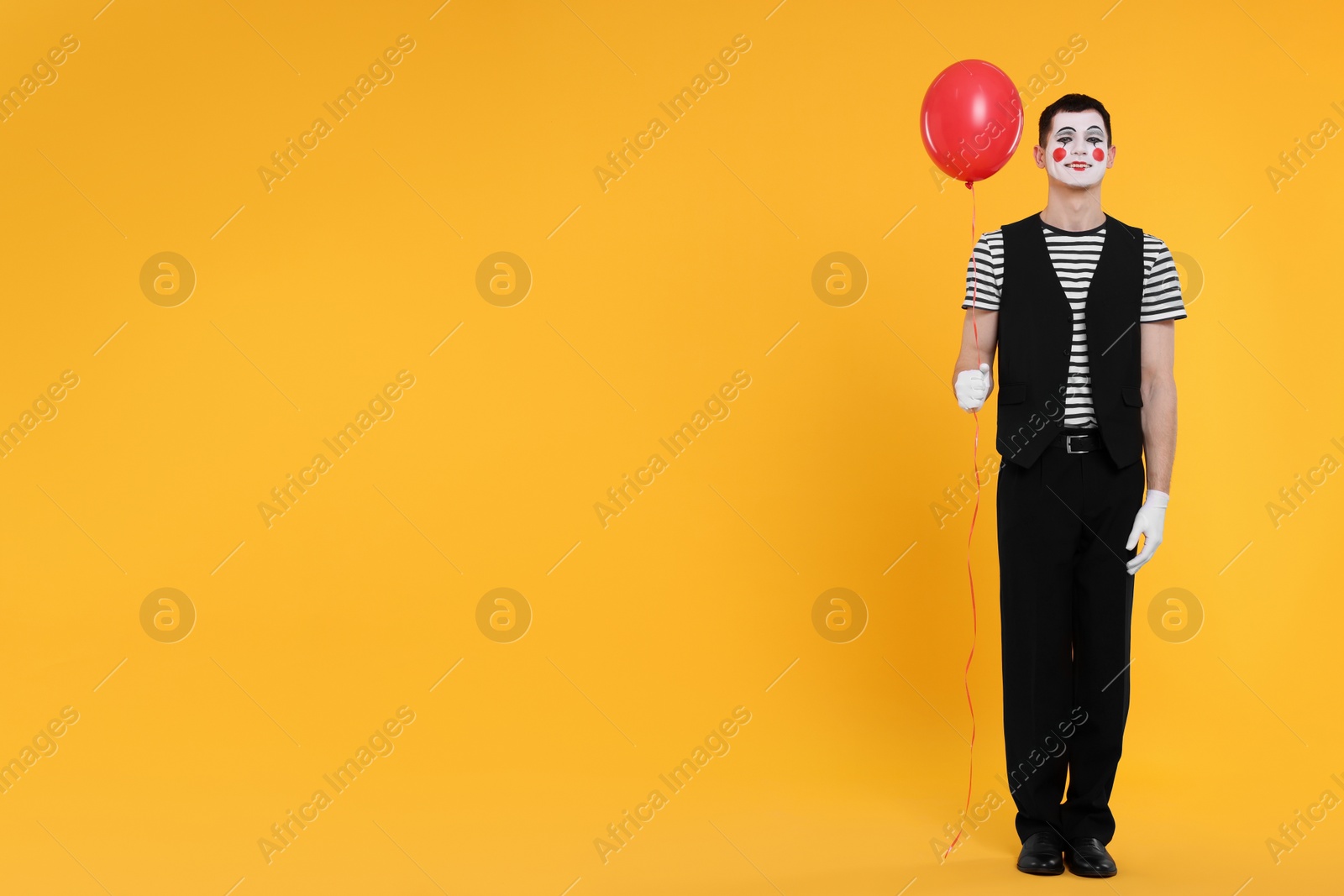 Photo of Funny mime artist with balloon on orange background. Space for text