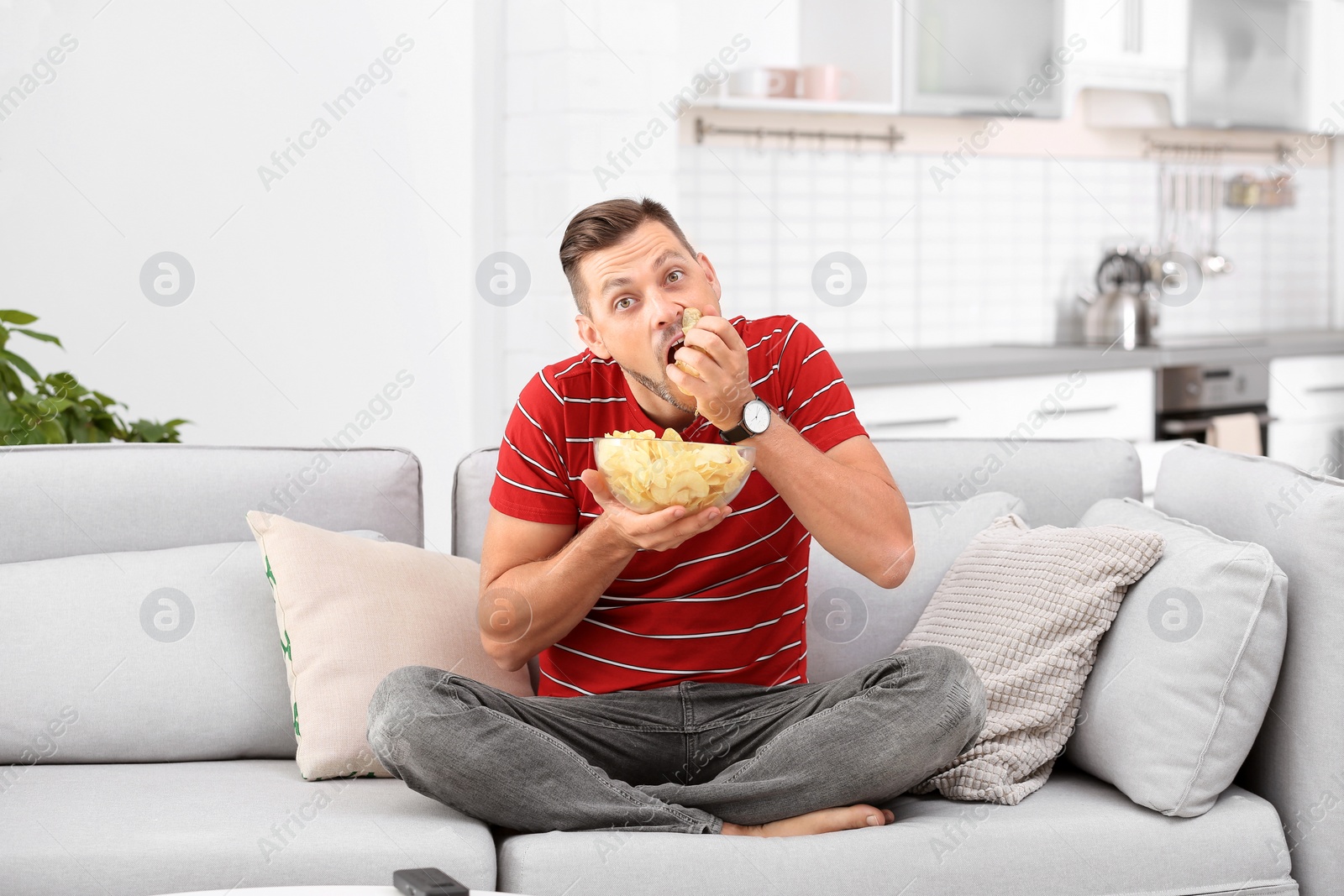 Photo of Man with bowl of potato chips sitting on sofa in living room