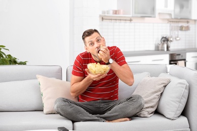 Man with bowl of potato chips sitting on sofa in living room