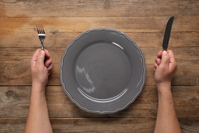Photo of Man with cutlery and empty plate at wooden table, top view