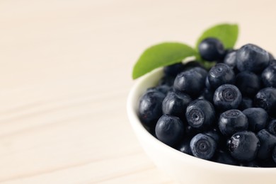 Photo of Tasty fresh bilberries with leaves in bowl on white table, closeup. Space for text