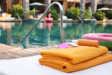 Beach towels, sunglasses and sunscreen on sun lounger near outdoor swimming pool at luxury resort, selective focus. Space for text