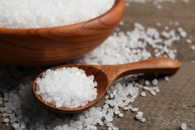 Photo of Bowl and spoon with sea salt on wooden table, closeup