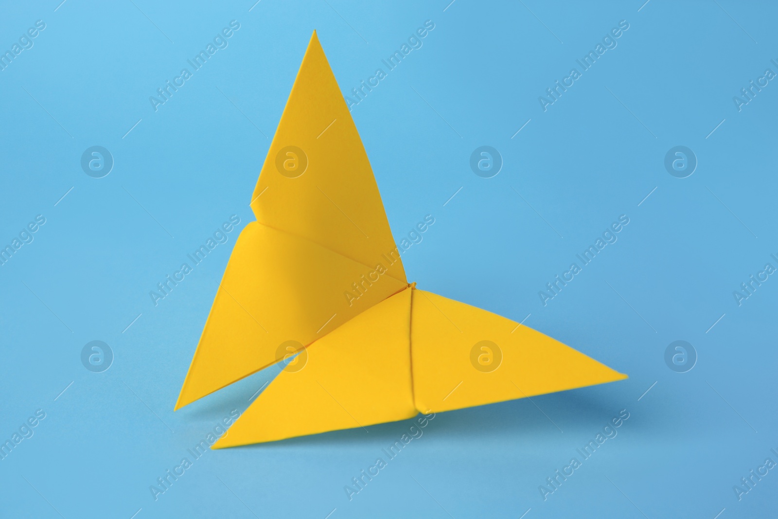 Photo of Origami art. Handmade yellow paper butterfly on light blue background