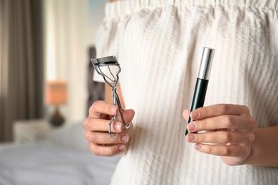 Photo of Woman holding mascara and eyelash curler indoors, closeup of hands. Space for text