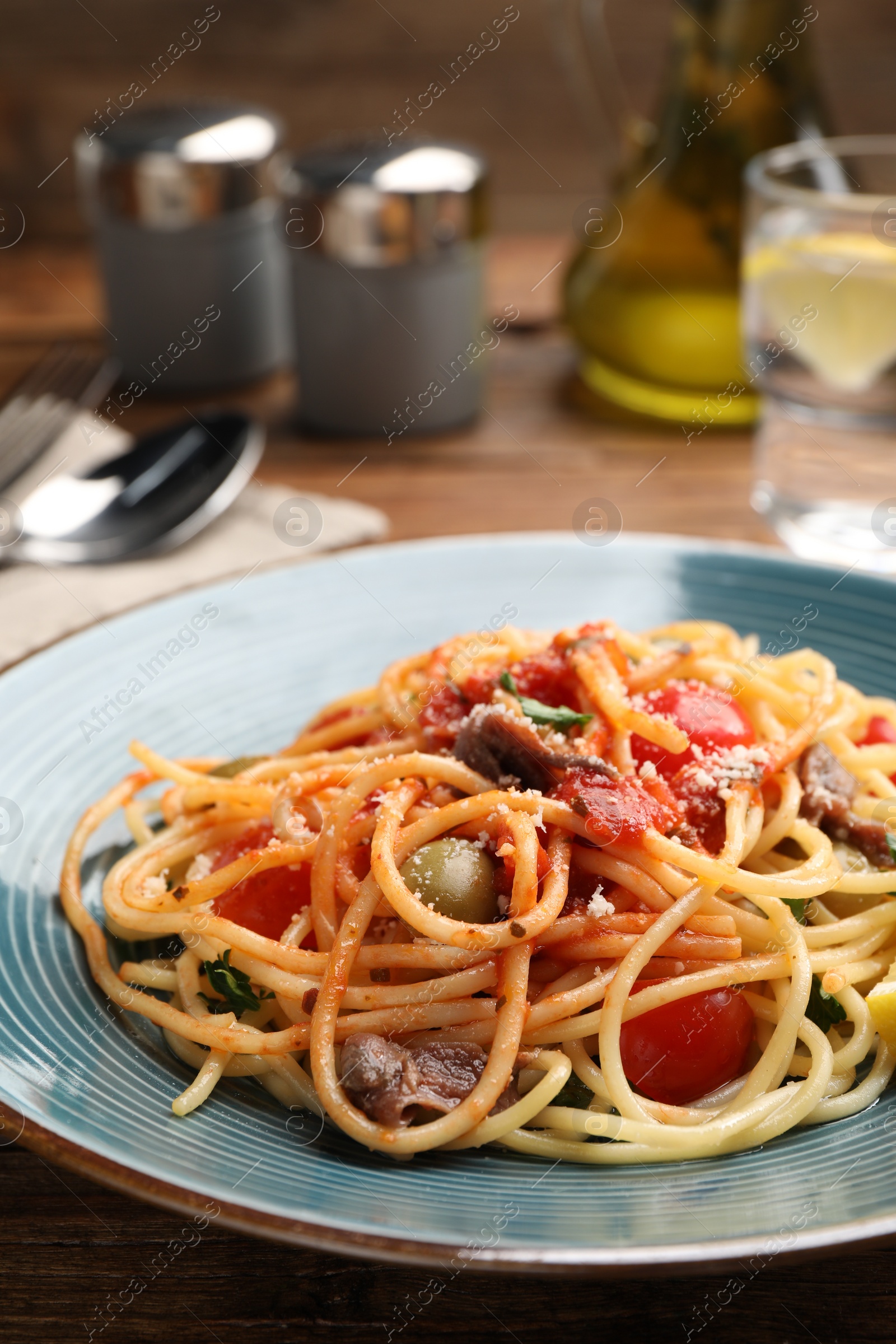 Photo of Delicious pasta with anchovies, tomatoes and parmesan cheese served on wooden table, closeup