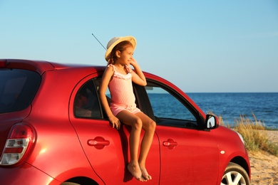 Photo of Little girl sitting on car window at beach. Summer trip
