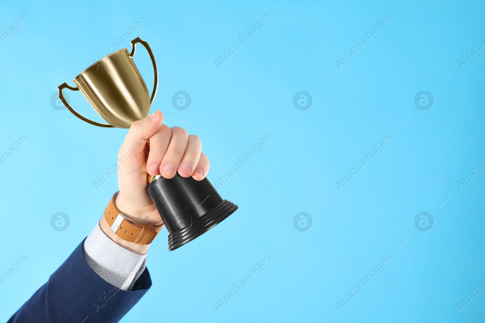 Photo of Businessman holding gold trophy cup on light blue background, closeup. Space for text