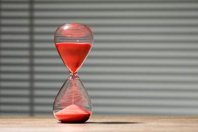 Hourglass with red flowing sand on wooden table against light background, space for text