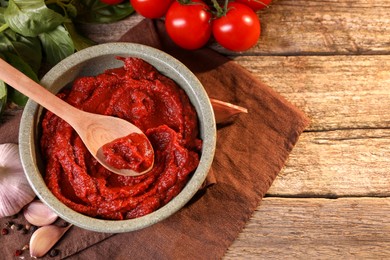 Photo of Bowl of tasty tomato paste with spoon and ingredients on wooden table, flat lay. Space for text