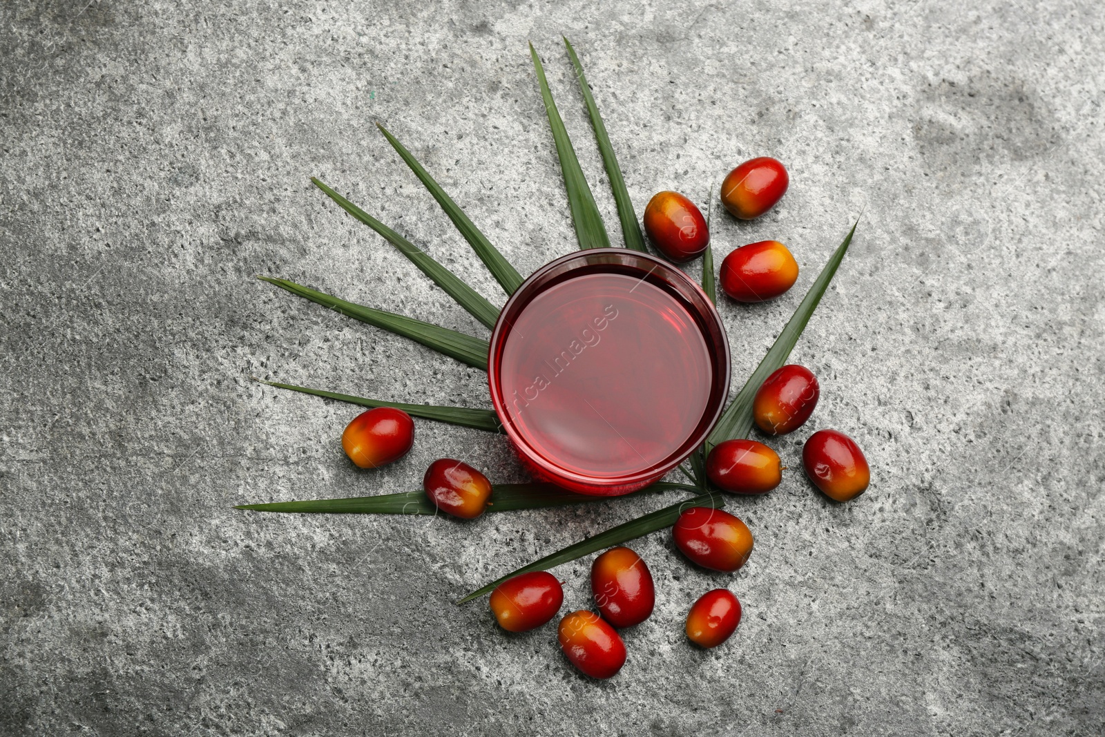 Photo of Palm oil in glass bowl, tropical leaf and fruits on grey table, flat lay